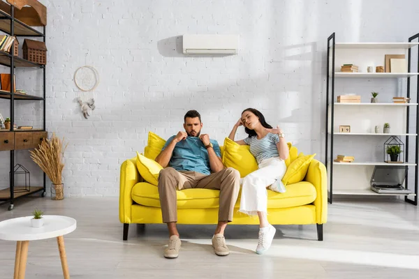 Selective focus of exhausted young couple feeling hot on couch in living room — Stock Photo