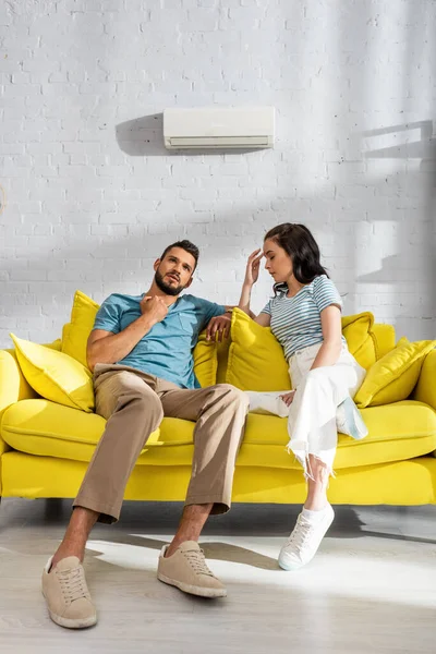 Young couple suffering from heat with air conditioner on wall at background in living room — Stock Photo