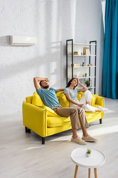 Man suffering from heat near tired girlfriend on sofa at home — Stock Photo