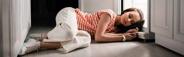 Panoramic crop of young woman sleeping on floor near open fridge in kitchen — Stock Photo