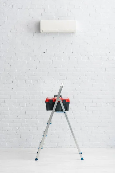 Caja de herramientas en escalera cerca de aire acondicionado en pared blanca - foto de stock