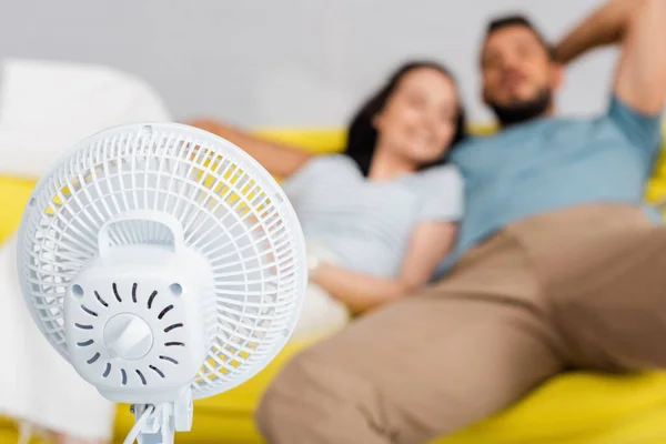 Enfoque selectivo de ventilador eléctrico cerca de pareja joven sentada en sofá - foto de stock