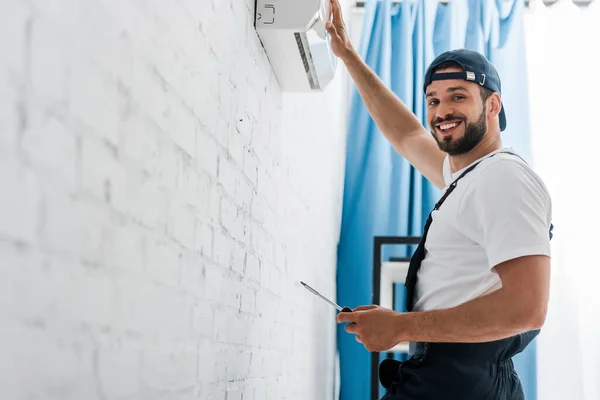 Lächelnder Arbeiter blickt bei der Reparatur einer Klimaanlage in die Kamera — Stockfoto