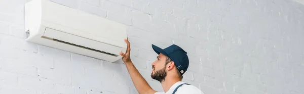 Panoramic crop of workman looking at air conditioner on wall — Stock Photo