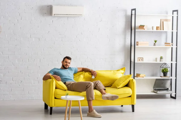 Bel homme barbu regardant la caméra tout en tenant télécommande de climatiseur dans le salon — Photo de stock