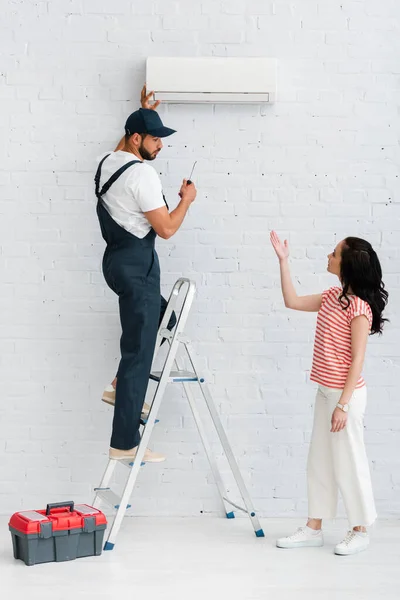 Vista lateral de la mujer apuntando con la mano cerca de trabajador de la fijación de aire acondicionado - foto de stock