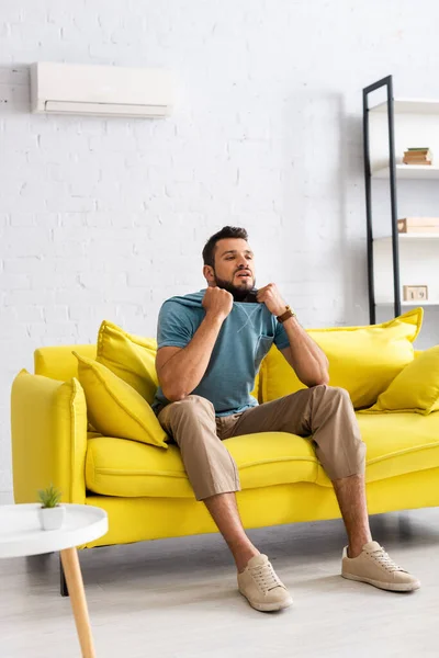 Selective focus of young man suffering from heat while sitting on sofa in living room — Stock Photo