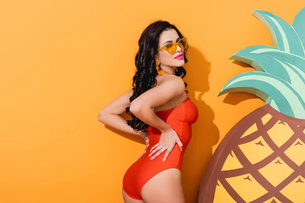 Приваблива жінка в купальнику і сонцезахисних окулярах стоїть біля паперу вирізала ананас на апельсині, літня концепція — стокове фото