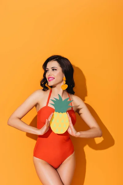 Happy woman in swimsuit holding paper cut pineapple on orange — Stock Photo