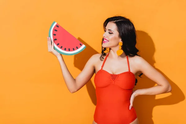 Lächelnde Frau im Badeanzug mit Blick auf Wassermelone auf Orange — Stockfoto