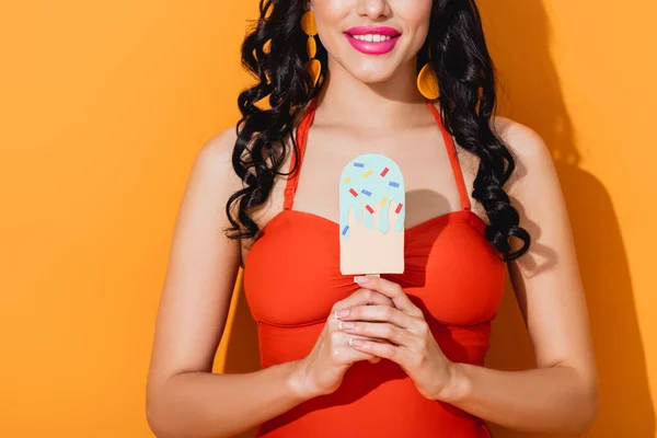 Cropped view of cheerful young woman holding paper cut ice cream on orange — Stock Photo
