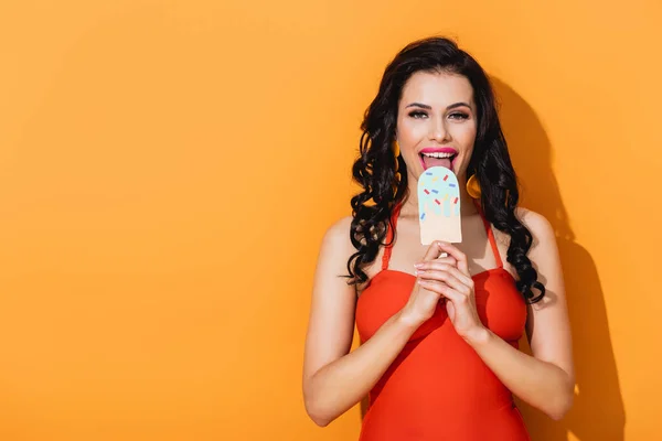 Heureuse jeune femme lécher le papier coupe crème glacée sur orange — Photo de stock