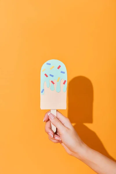 Vue recadrée de la femme tenant de la crème glacée coupée en papier sur orange — Photo de stock