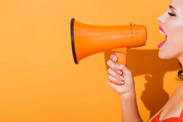 Side view of young woman screaming in megaphone on orange — Stock Photo