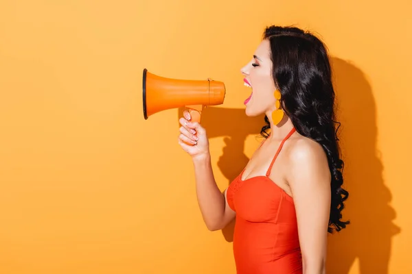 Profile of young woman in swimsuit screaming in megaphone on orange — Stock Photo