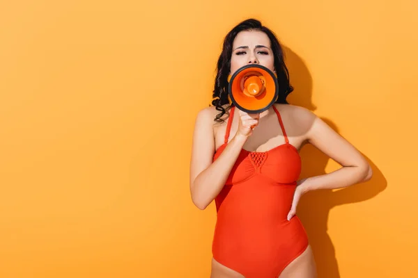 Giovane donna in piedi con mano sul fianco e urlando in megafono su arancione — Foto stock