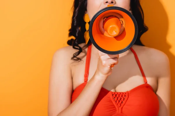 Cropped view of young woman screaming in megaphone on orange — Stock Photo