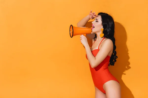 Animado jovem mulher em maiô segurando megafone em laranja — Fotografia de Stock