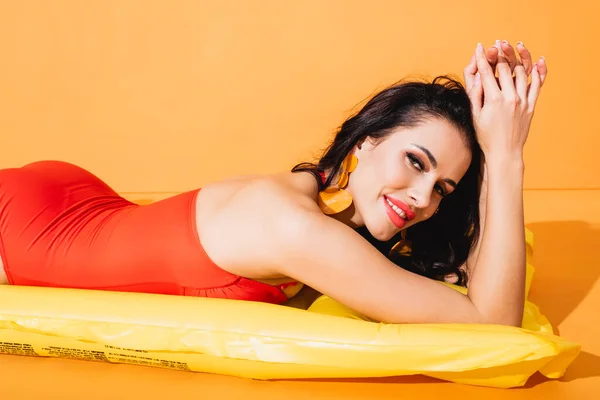 Happy girl in swimsuit lying on inflatable mattress on orange — Stock Photo