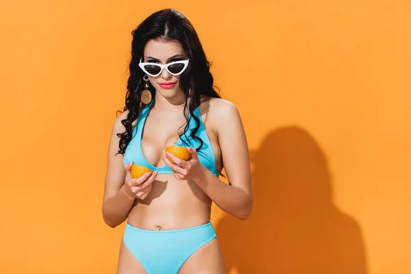 Elegante donna in costume da bagno e occhiali da sole con frutta biologica a metà su arancione — Foto stock