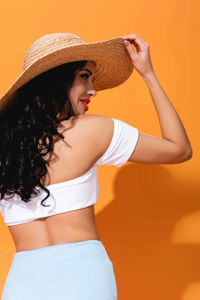Веселая и стильная девушка в соломенной шляпе, стоящая на оранжевом — стоковое фото