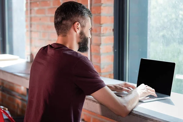 Hombre de negocios barbudo utilizando el ordenador portátil con pantalla en blanco en la oficina moderna - foto de stock