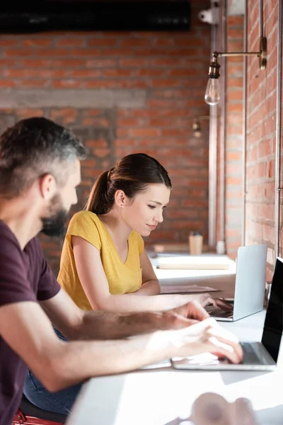 Enfoque selectivo de la atractiva mujer de negocios y hombre de negocios utilizando computadoras portátiles en la oficina - foto de stock