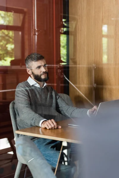 Вибірковий фокус бородатого бізнесмена, що сидить за столом з ноутбуком — стокове фото