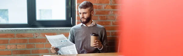 Panoramic orientation of bearded businessman holding paper cup and reading newspaper — Stock Photo
