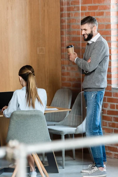 Foco seletivo de empresário feliz segurando copo de papel e olhando para colega de trabalho — Fotografia de Stock