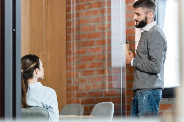 Selective focus of handsome businessman holding paper cup and looking at coworker — Stock Photo