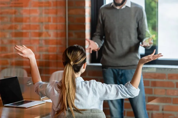 Vista posterior de la mujer de negocios sentada y gesticulando cerca de compañero de trabajo en la oficina - foto de stock