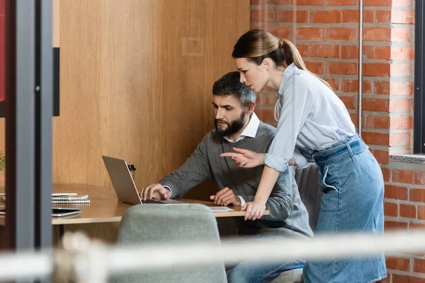 Selective focus of businesswoman pointing with finger at laptop near coworker — Stock Photo