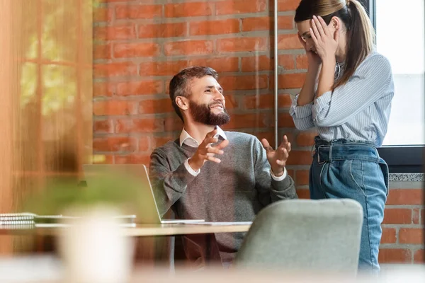 Selektiver Fokus einer glücklichen Geschäftsfrau, die ihr Gesicht in der Nähe eines fröhlichen Mitarbeiters im Büro verdeckt — Stockfoto