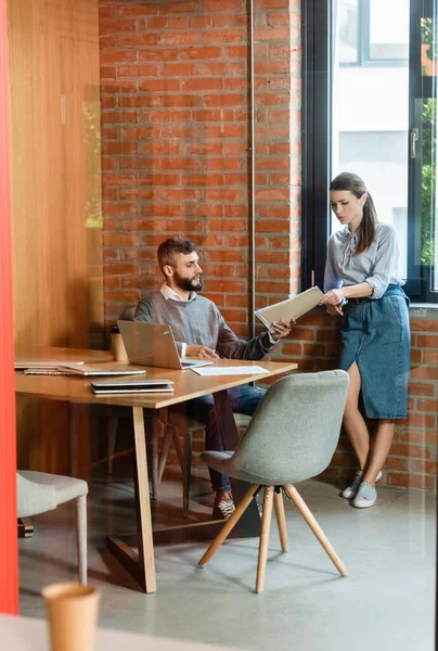 Enfoque selectivo de atractiva mujer de negocios y apuesto empresario de cartera en la oficina - foto de stock