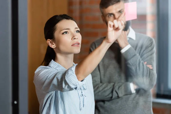 Enfoque selectivo de la mujer de negocios que apunta con el dedo a la nota adhesiva cerca de hombre de negocios - foto de stock