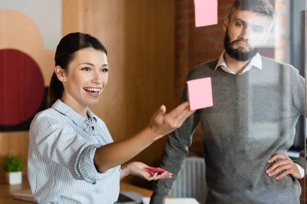 Enfoque selectivo de la mujer de negocios feliz señalando con la mano en la nota pegajosa cerca de hombre de negocios - foto de stock