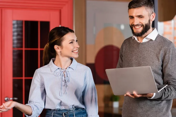 Femme d'affaires joyeux geste tout en regardant bel homme avec ordinateur portable au bureau — Photo de stock