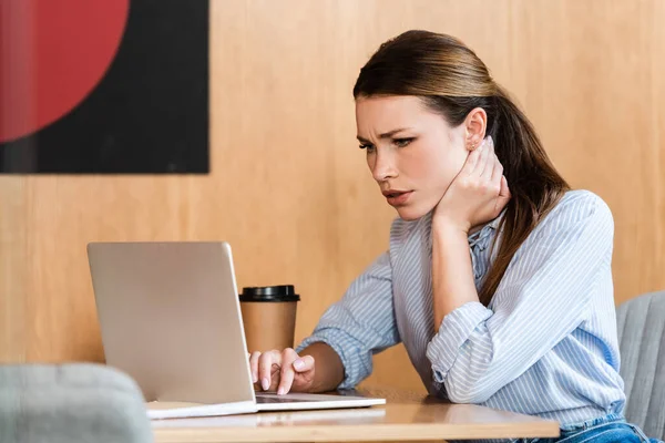Selektive Fokussierung gestresster Geschäftsfrau mit Laptop in der Nähe von Pappbechern — Stockfoto