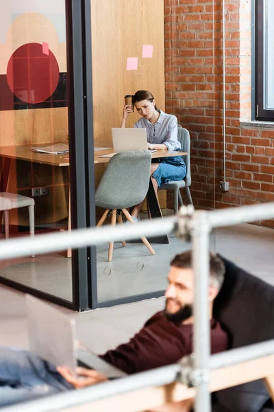 Foyer sélectif de femme d'affaires en utilisant un ordinateur portable près de l'homme d'affaires dans le bureau moderne — Photo de stock