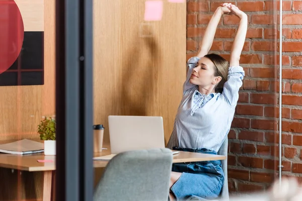 Selective focus of businesswoman stretching near laptop and paper cup — Stock Photo