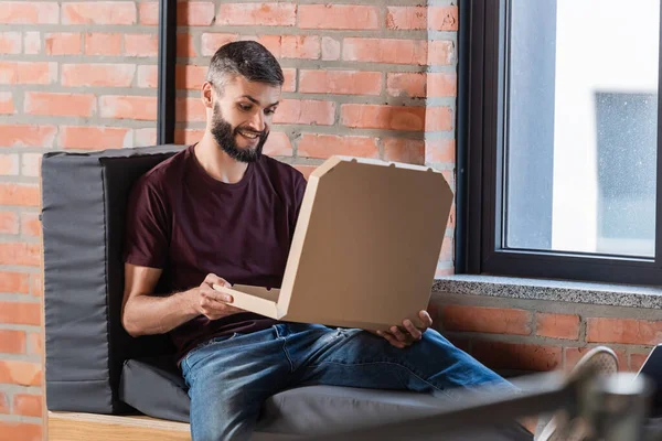 Selective focus of cheerful businessman sitting on window bench and holding carton pizza box — Stock Photo