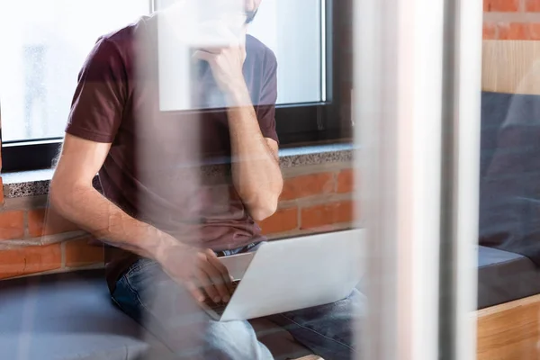 Cropped view of businessman sitting on window bench and using modern laptop — Stock Photo