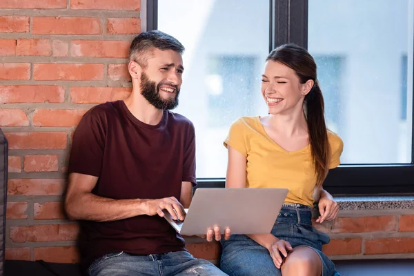 Mulher de negócios feliz e empresário barbudo sorrindo perto do laptop no escritório — Fotografia de Stock