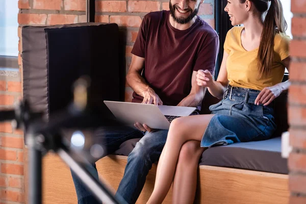 Enfoque selectivo de la mujer de negocios feliz y hombre de negocios barbudo sentado en el banco de la ventana con el ordenador portátil - foto de stock