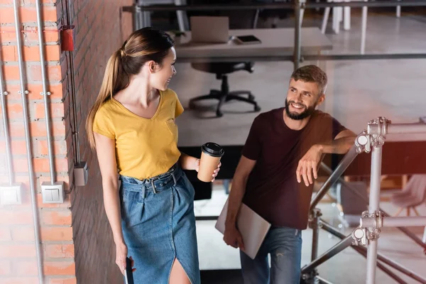 Focus selettivo di attraente donna d'affari con tazza di carta guardando uomo d'affari con laptop — Foto stock