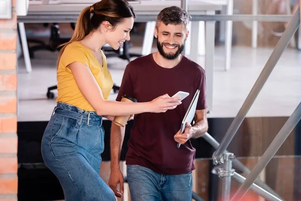 Zufriedene Mitarbeiter, die im Büro aufs Smartphone schauen — Stockfoto