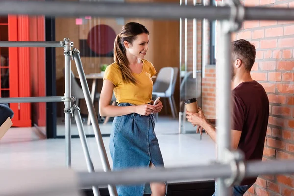 Selektiver Fokus attraktiver Geschäftsfrau, die Geschäftsfrau mit Pappbecher und Smartphone anschaut — Stockfoto