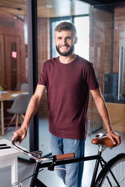 Счастливый бизнесмен, стоящий с велосипедом в современном офисе — стоковое фото