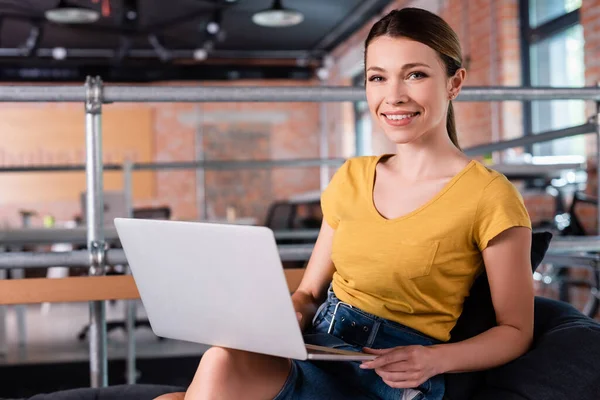 Felice donna d'affari utilizzando il computer portatile mentre seduto sul divano in ufficio moderno — Foto stock
